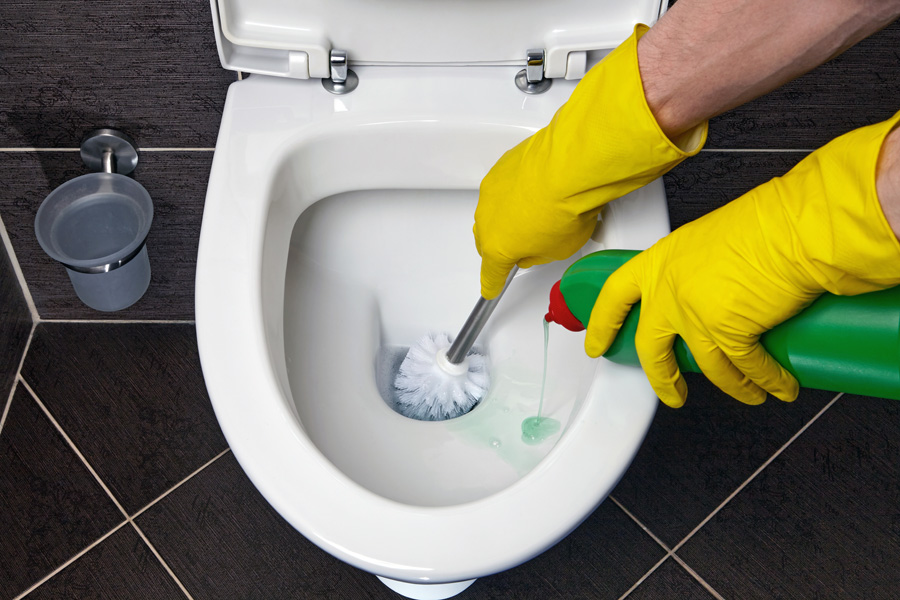 Toilet cleaning and disinfection. Cleaner in yellow rubber gloves cleans the toilet bowl with a brush and disinfectant